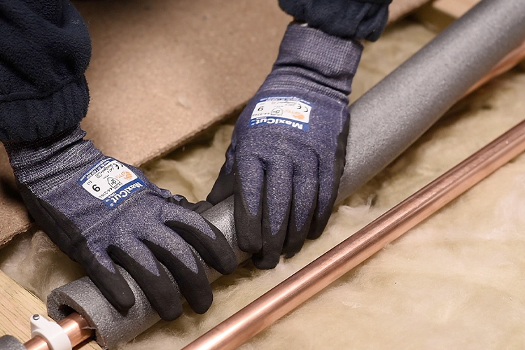 A person cutting pipe lagging to fit pipes in a loft