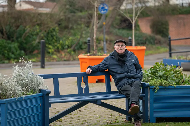 John Boaler, Chair of Calne Pocket Park sat on a bench with his new tree planters in the background.